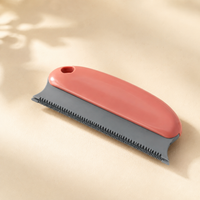 Reusable pet hair remover scraper in coral and grey on a warm neutral background